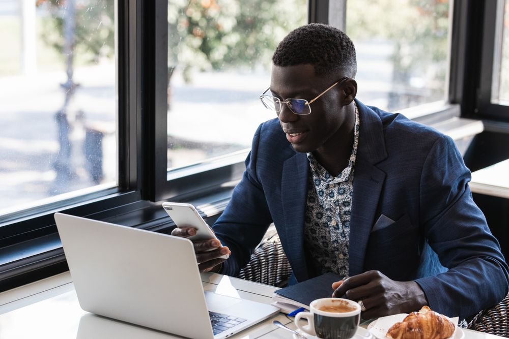 Stylish Black executive with smartphone and laptop in cafe