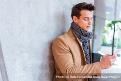 Man in camel coat and scarf looking at phone outside 5lVEQV