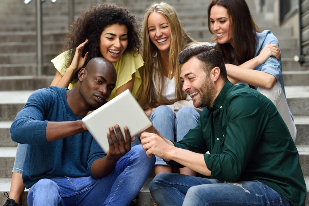 Men and women engaged by something on digital tablet while sitting on outdoor cement staircase