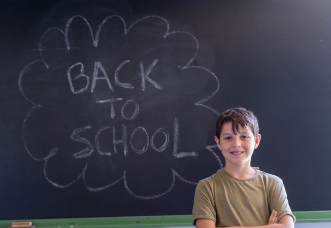 Smiling boy standing at board with "back to school" written in chalk