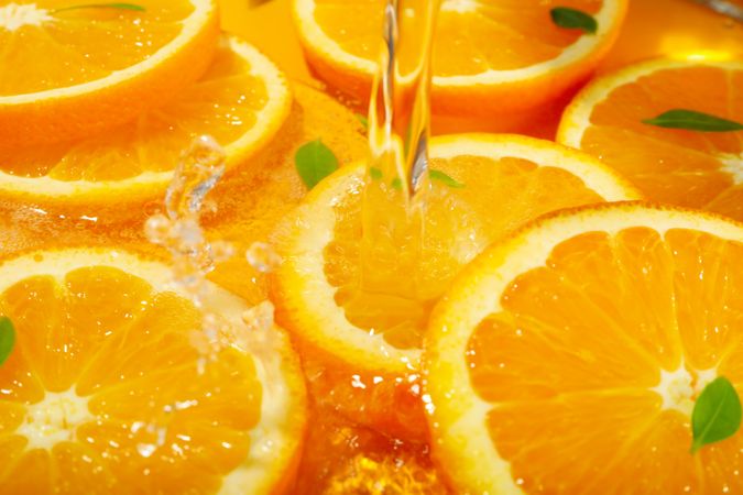 Water being poured on fresh orange slices with leaves