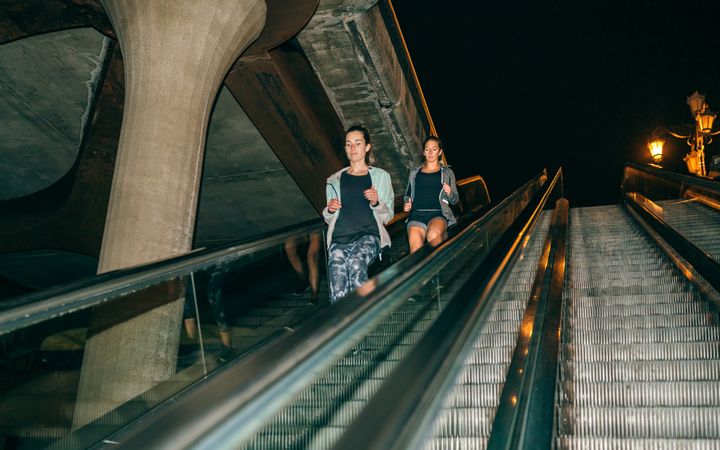 Female friends running down escalator in city at night
