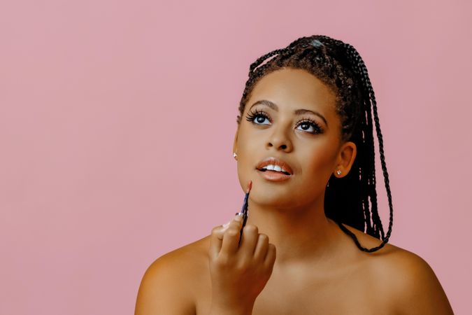 Calm Black woman holding lip gloss while looking up