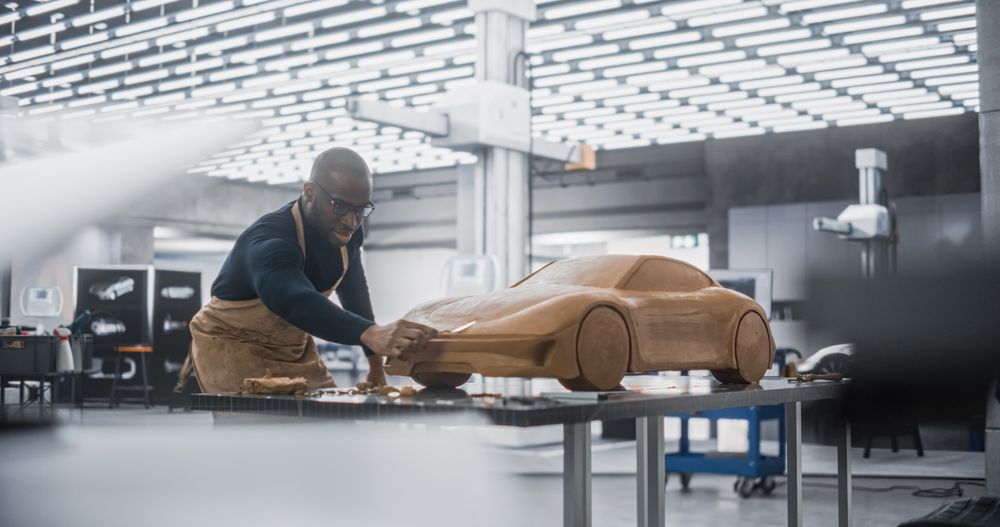 Black Designer Working on a New Prototype, Sculpting Industrial Plasticine Clay 3D Model of a Sporty Coupe.