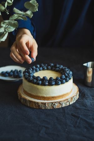 Person’s hand adding blueberry to cheesecake
