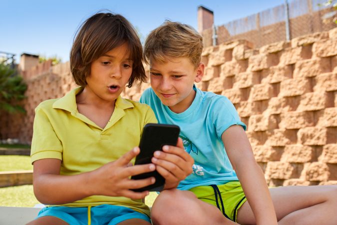Cheerful boys browsing smartphone on sunbed