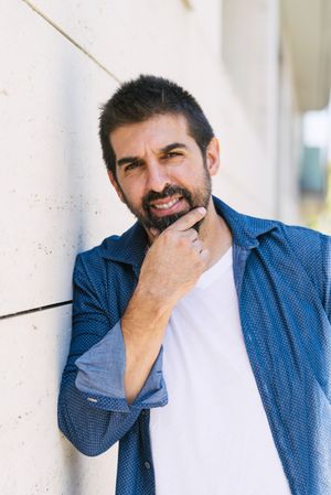 Man in denim standing outside holding beard deep in thought