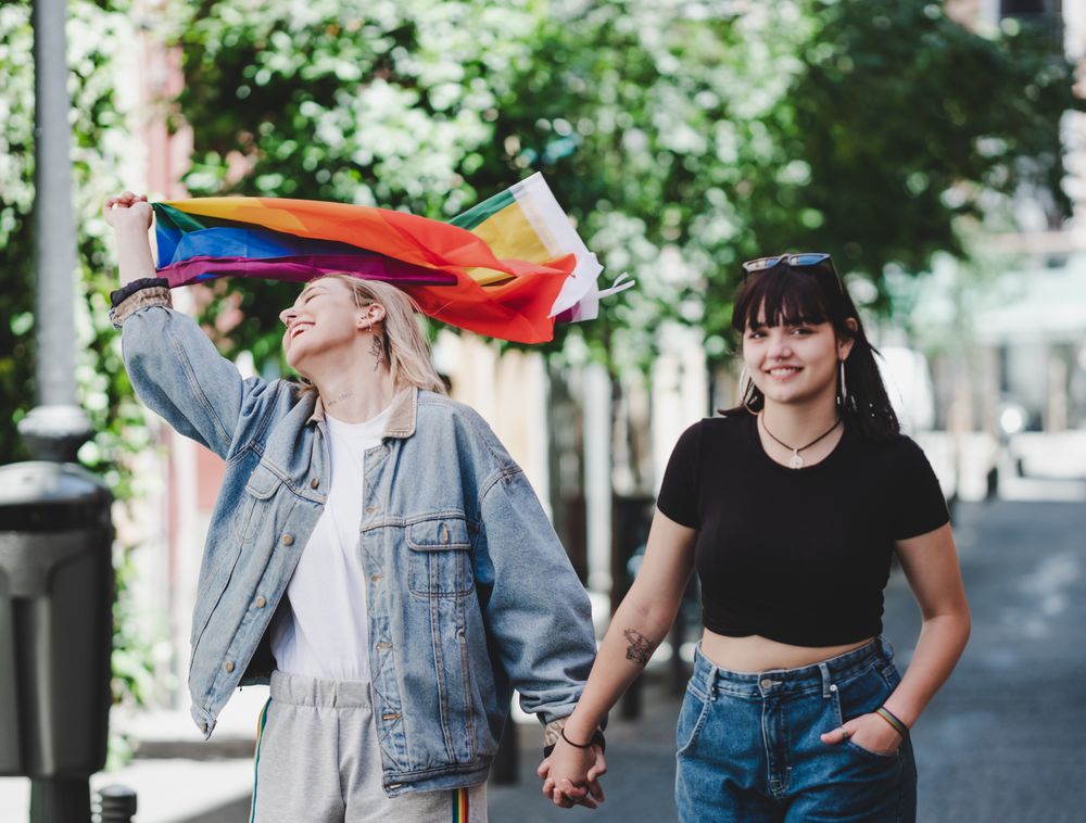 Lesbian couple with LGBT flag walking on street