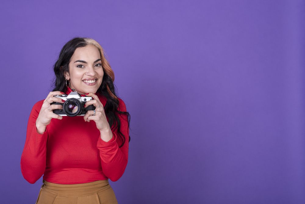 woman taking a photo with her film camera over a violet background. Copy space.