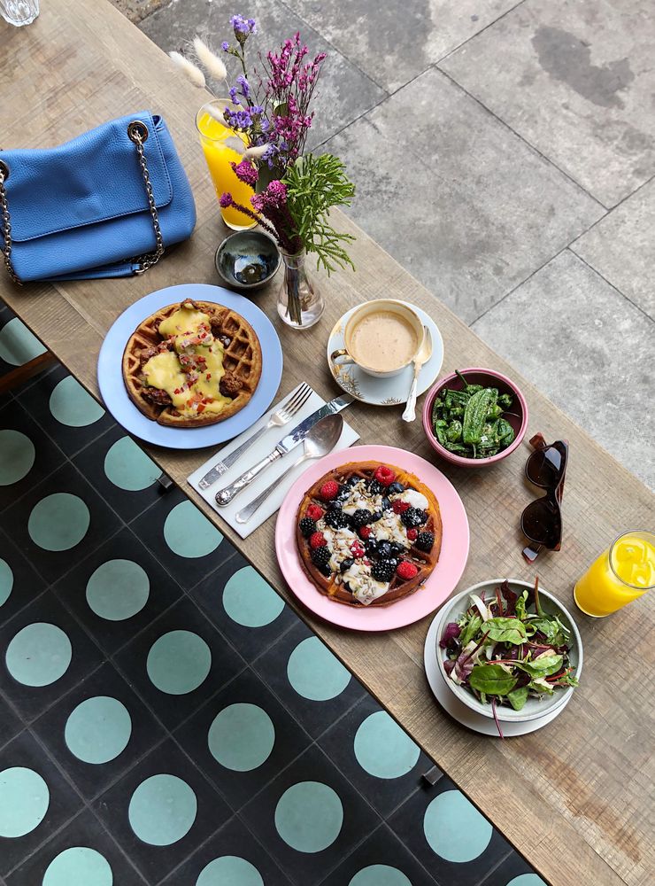 Top view of two waffle plates and salad beside cup of coffee and orange juice