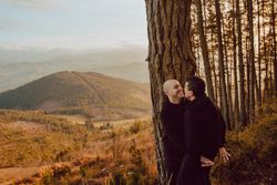 Smiling men hugging near tree in forest on hill