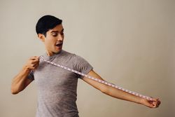 Surprised Hispanic male holding measuring tape down to his side in beige studio shoot