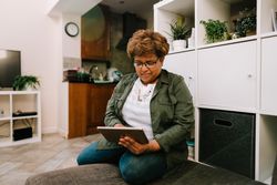 Smiling older Black woman sitting on sofa reading from tablet