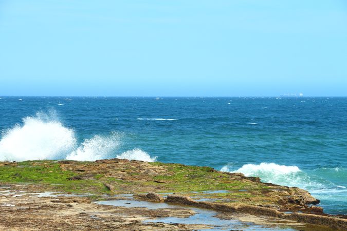 Waves Crashing On Rocky Shoreline With Green Moss And Clear Blue Ocean On A Bright Day
