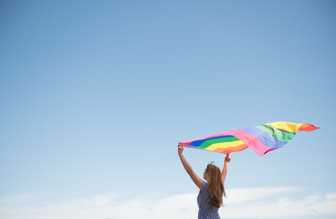 Young woman with rainbow banner against sky