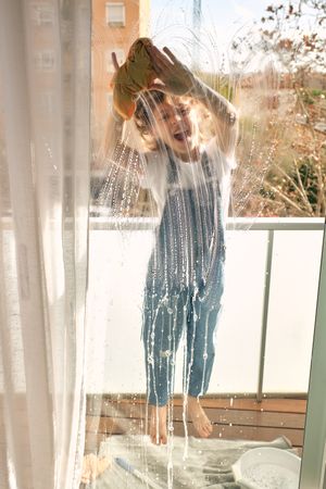 Cheerful boy washing windows with rag at home