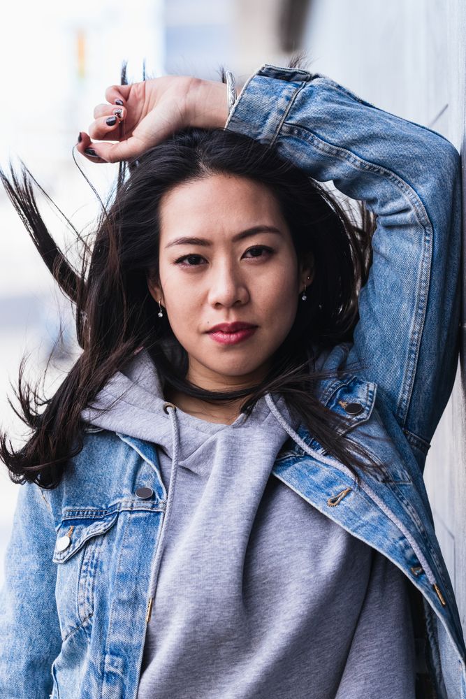 Asian brunette woman with long hair leaning on the wall and looking at camera