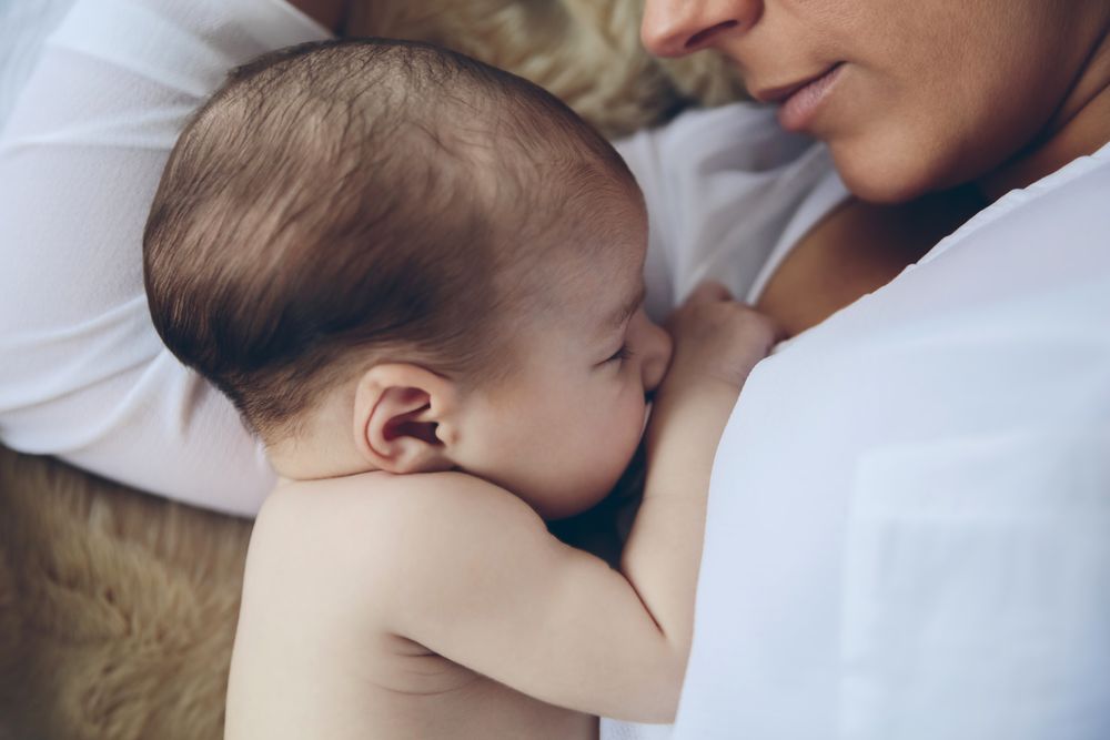 Newborn lying on the bed embraced by her mother