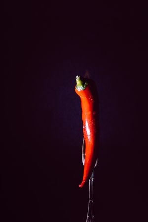 red chili pepper on fire in fork on a dark background