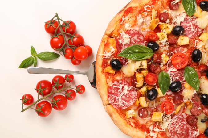 Tasty pizza, basil, tomatoes and shovel on plain background, top view