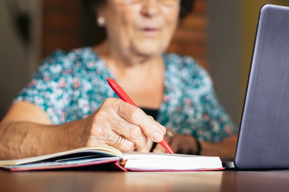 Older woman using a laptop and a notebook at home