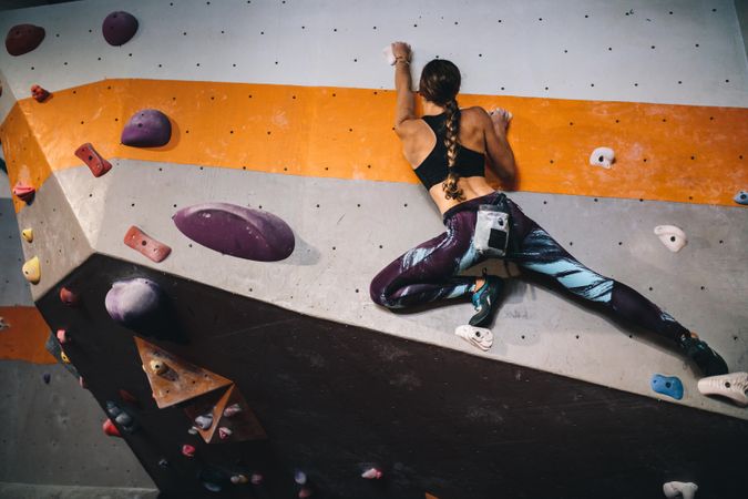 Athletic woman wearing climbing gear and rock climbing at gym