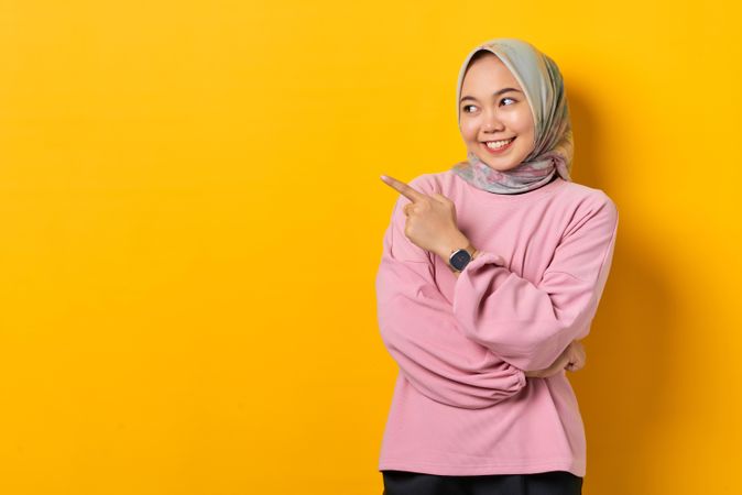 Smiling Muslim woman in headscarf pointing to space beside her