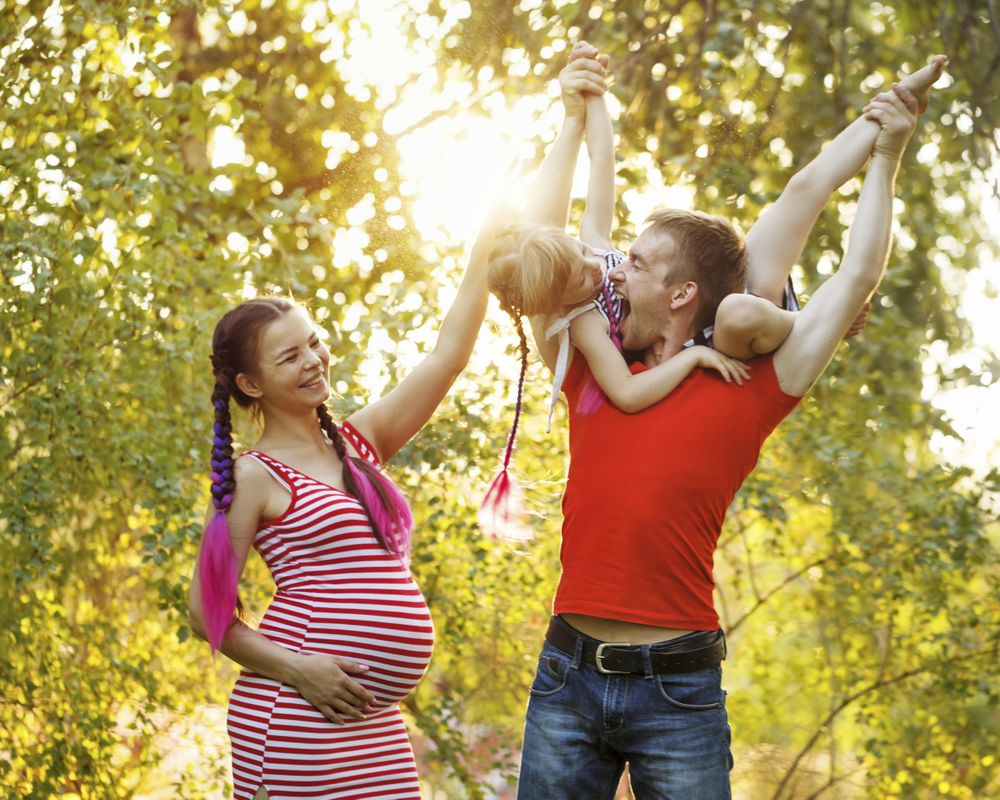 Playful father lifting daughter above his head in sunny park under trees