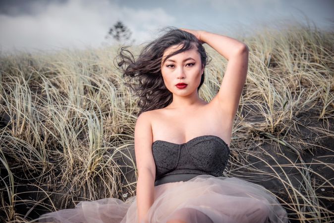 Portrait of young woman in dark dress sitting on brown grass
