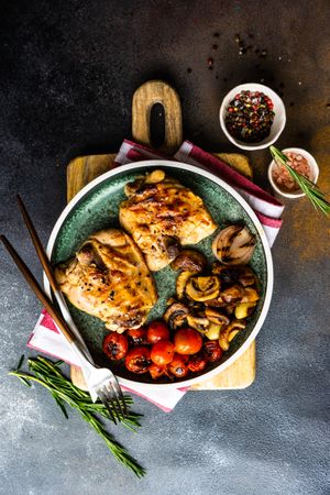 Top view of plate of grilled chicken and vegetable on stone background