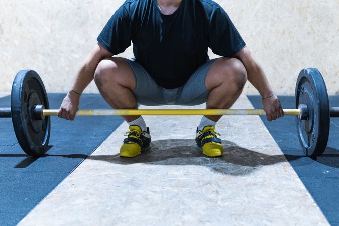 Unrecognizable sportsman lifting barbell in gym