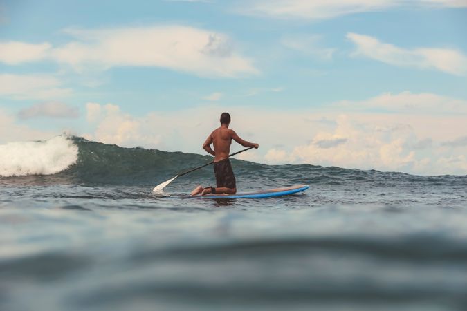 Man with paddle on surf board waving on water