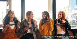 Female friends sitting in cafe holding a cup of coffee and smiling 56lNNb