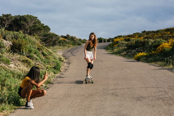 Hispanic woman taking photo of friend balancing on longboard