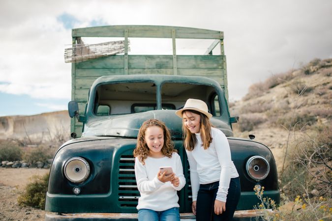Cheerful girls watching smartphone near abandoned truck