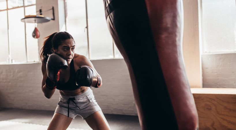 Fit female boxer using a punching bag with gloves inside a boxing ring