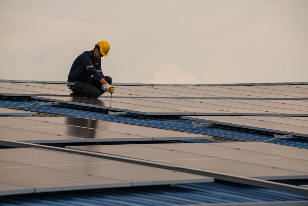 Engineer worker using electric drill repairing on solar cell panel on the roof of the factory. After service and security for industrial renewable energy concept