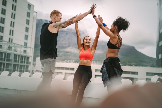 Three fitness people standing on rooftop after workout holding their hands in joy