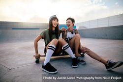 Two female friends sitting on a long board and laughing 49OLv0