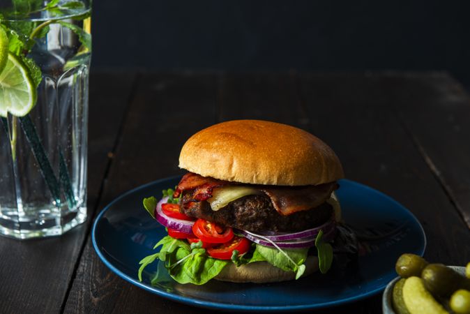 Burger on a blue plate glass of water and pickels