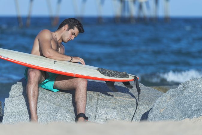 Male surfer relaxing near sea with board on lap