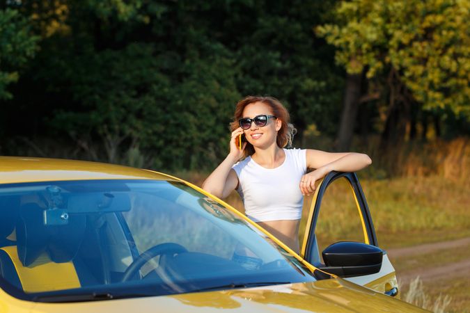 Woman talking on cell phone standing outside of her yellow car