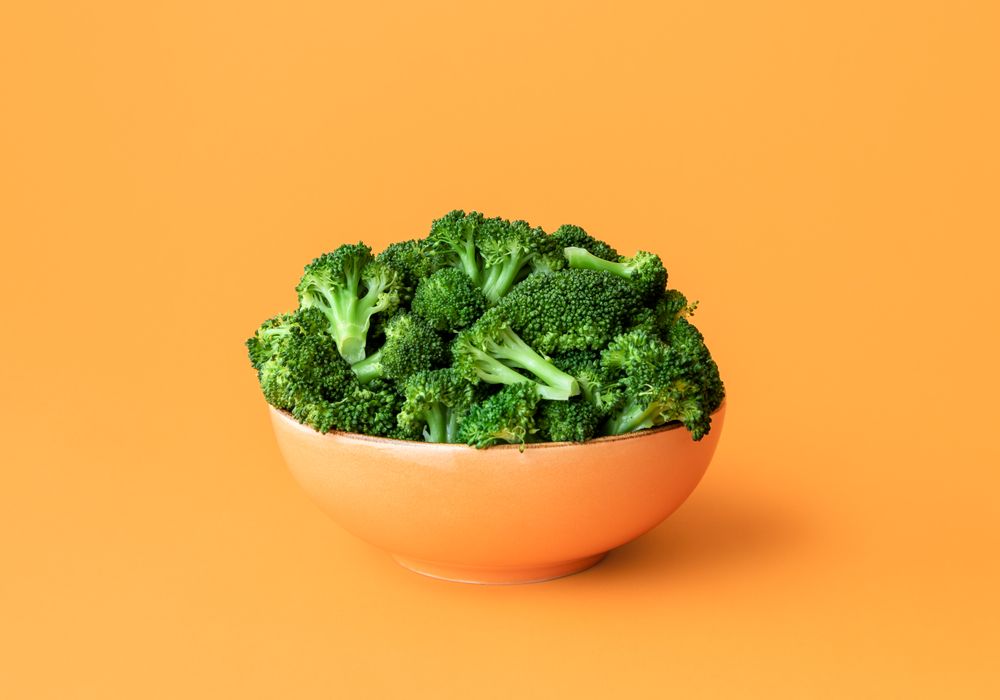 Cooked broccoli in a bowl isolated on an orange background
