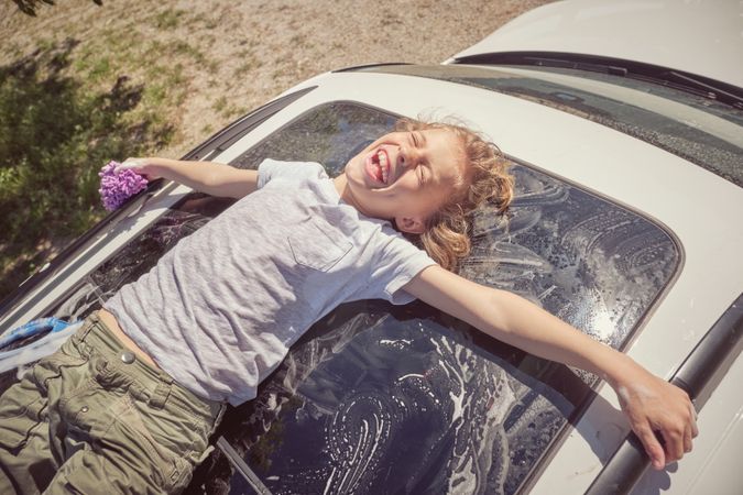 Joyful boy lying on white car window while resting after washing