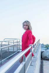 Side of woman in red coat leaning on railing of foot bridge