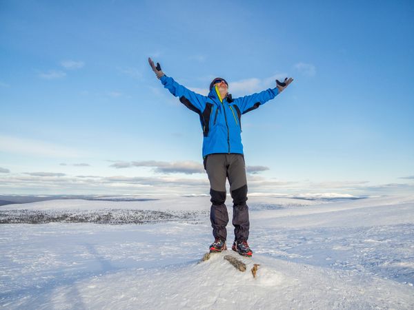 Man with arms raised standing in the snow on wintry day