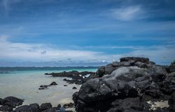 Dark lava rocks on the beach before the crystal waters of the Indian Ocean