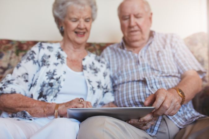 Portrait of happy older couple sitting together at home and using digital tablet