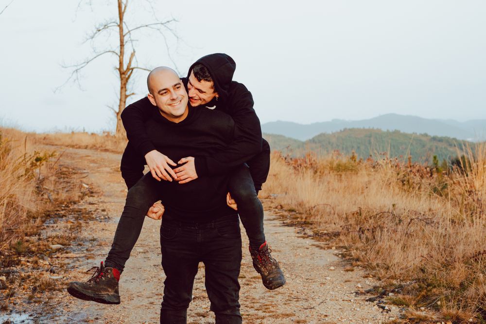 Smiling man holding on back cheerful guy on road on hill