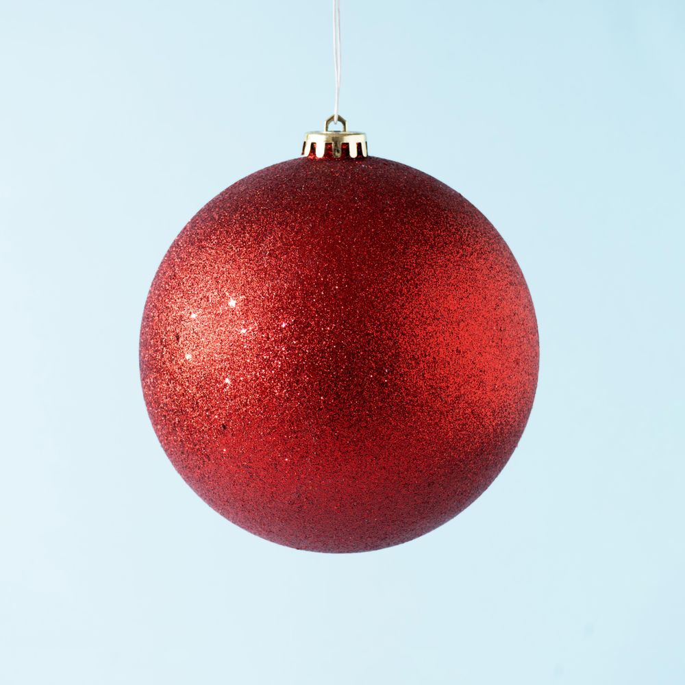 Red glitter Christmas bauble on pastel blue background